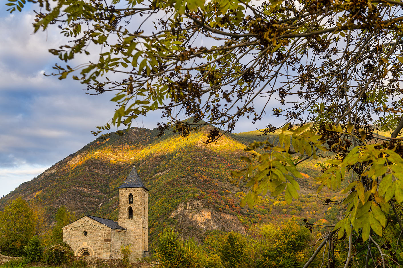Vista exterior de l’església de l’Assumpció de Cóll amb les muntanyes al fons.