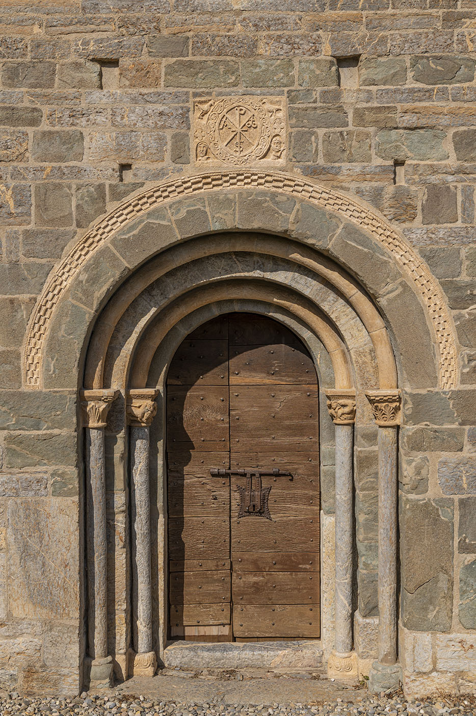 Portalada de l’església de l’Assumpció de Cóll amb columnes rematades amb arcs i el crismó al damunt.