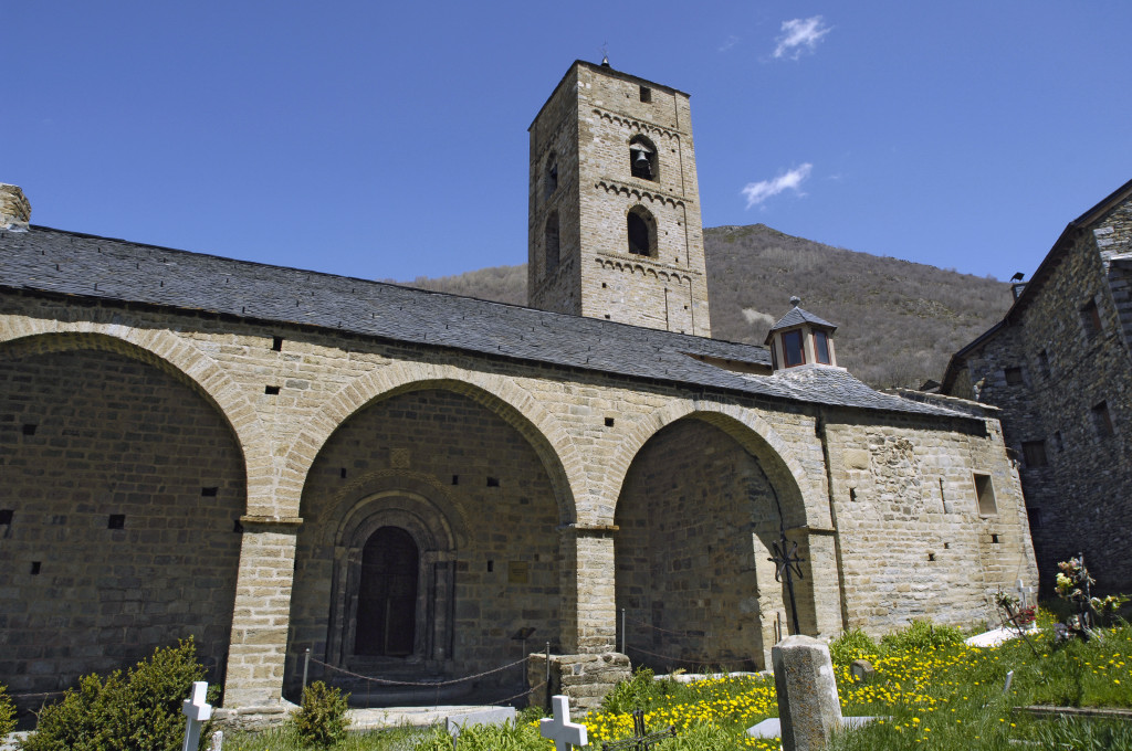 Porxo de l’església de la Nativitat de Durro amb el campanar al darrere i les creus de les tombes en primer terme.