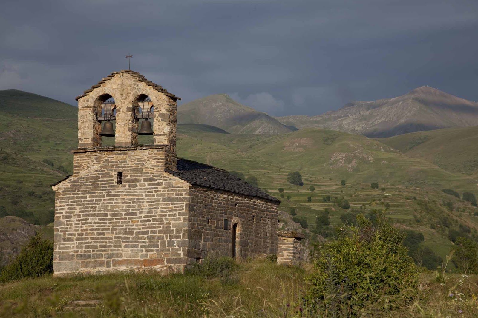 Exterior de l’ermita de Sant Quirc de Durro coronada pel campanar d’espadanya i envoltada de muntanyes.