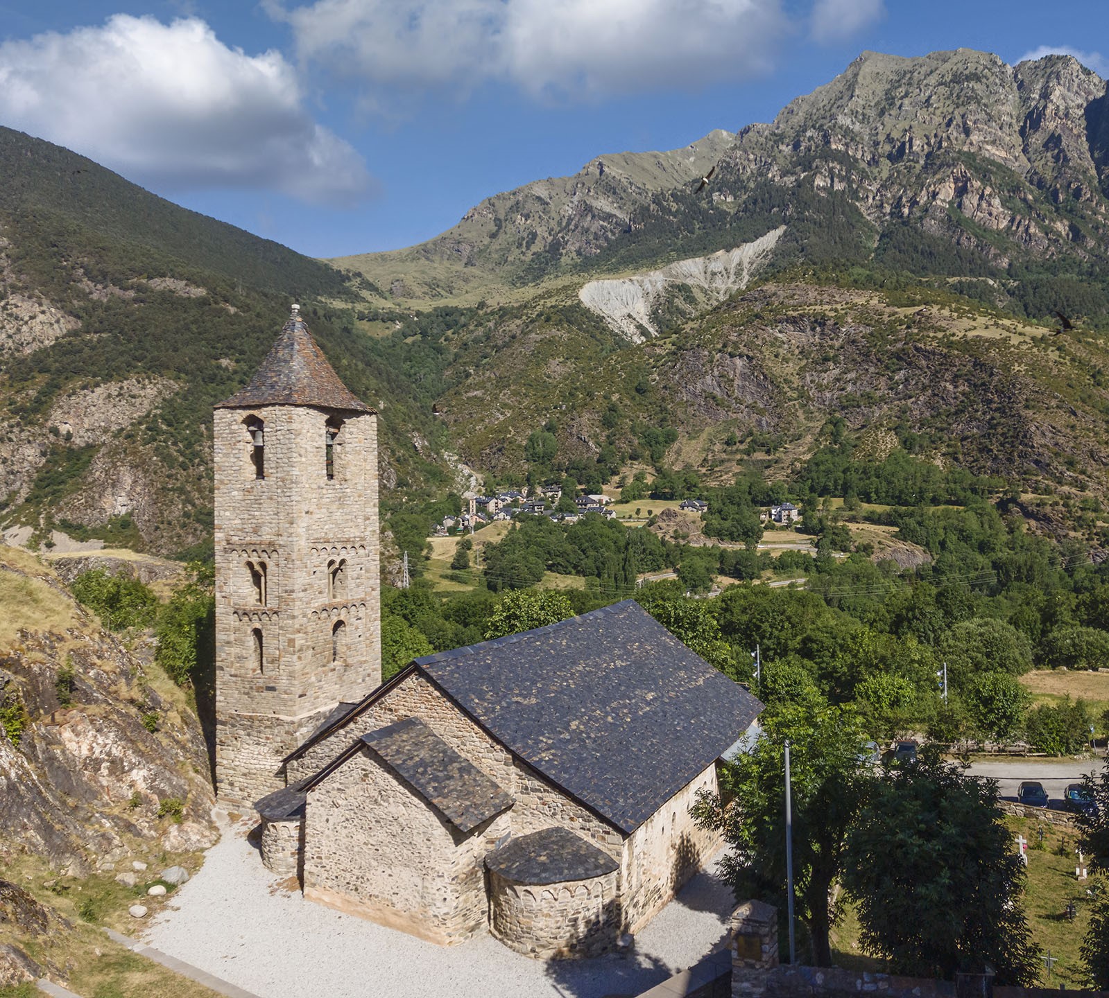 Vista exterior de l’església de Sant Joan de Boí des de la part posterior, amb les muntanyes al fons.