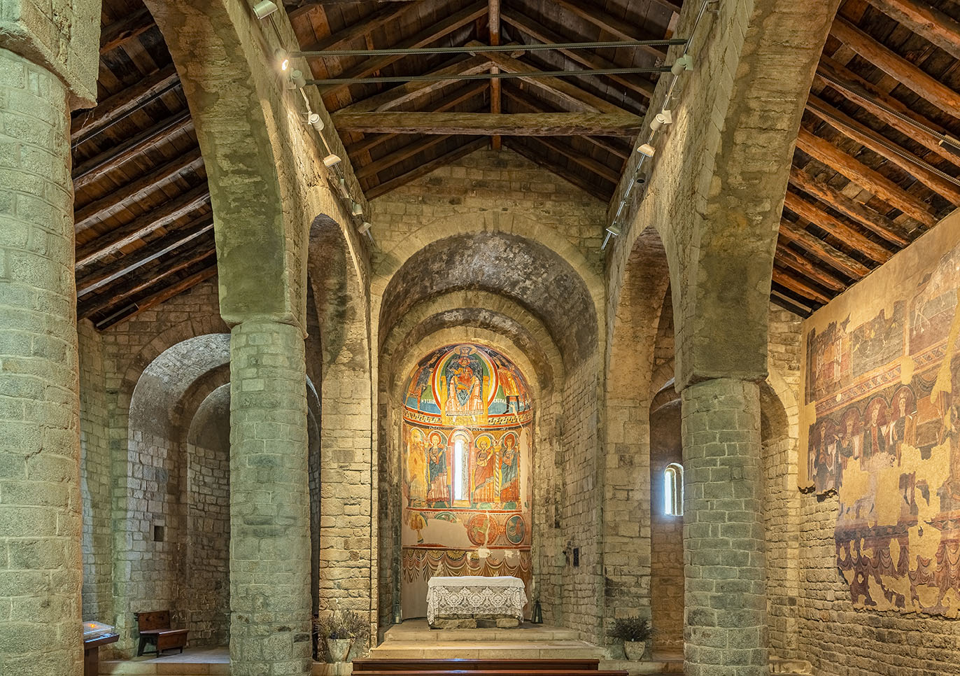 Vista general interior de les tres naus de l’església de Santa Maria de Taüll amb les pintures de l’absis principal al fons i les del mur sud a la dreta.