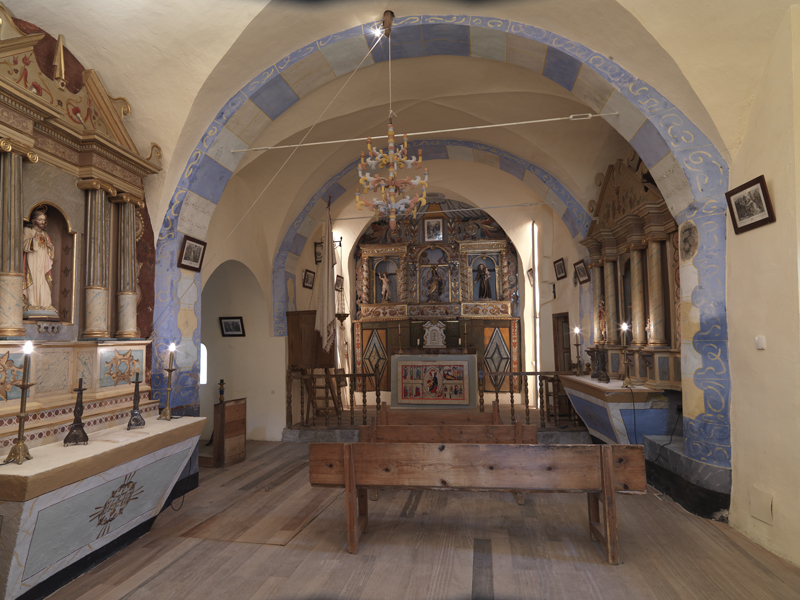 Interior de l’església de Santa Maria de Cardet amb els murs encalcinats i amb l’altar i el retaule al fons.