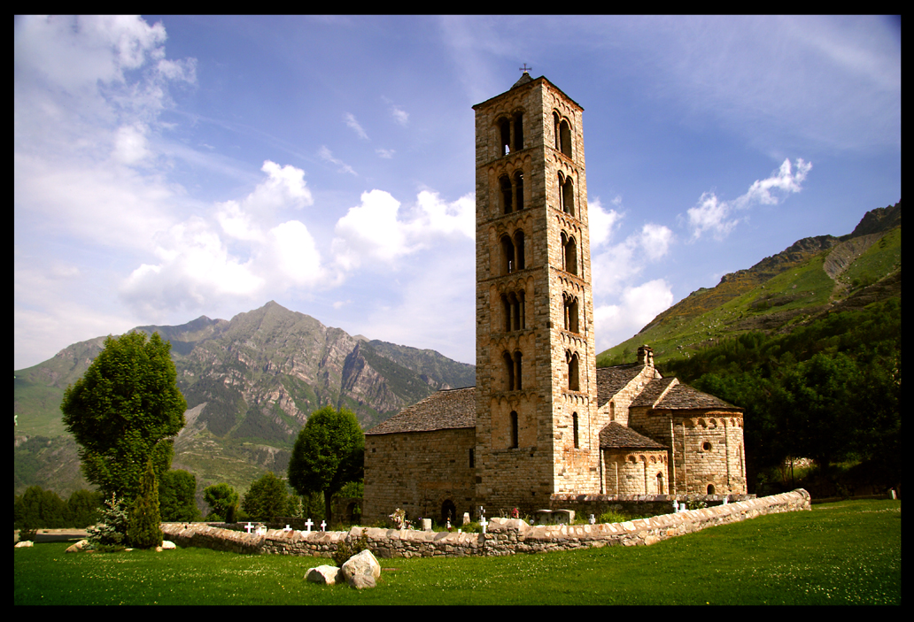 Vista general de l’exterior de l’església de Sant Climent de Taüll, amb el cementiri i la torre del campanar en primer terme i les muntanyes al fons.
