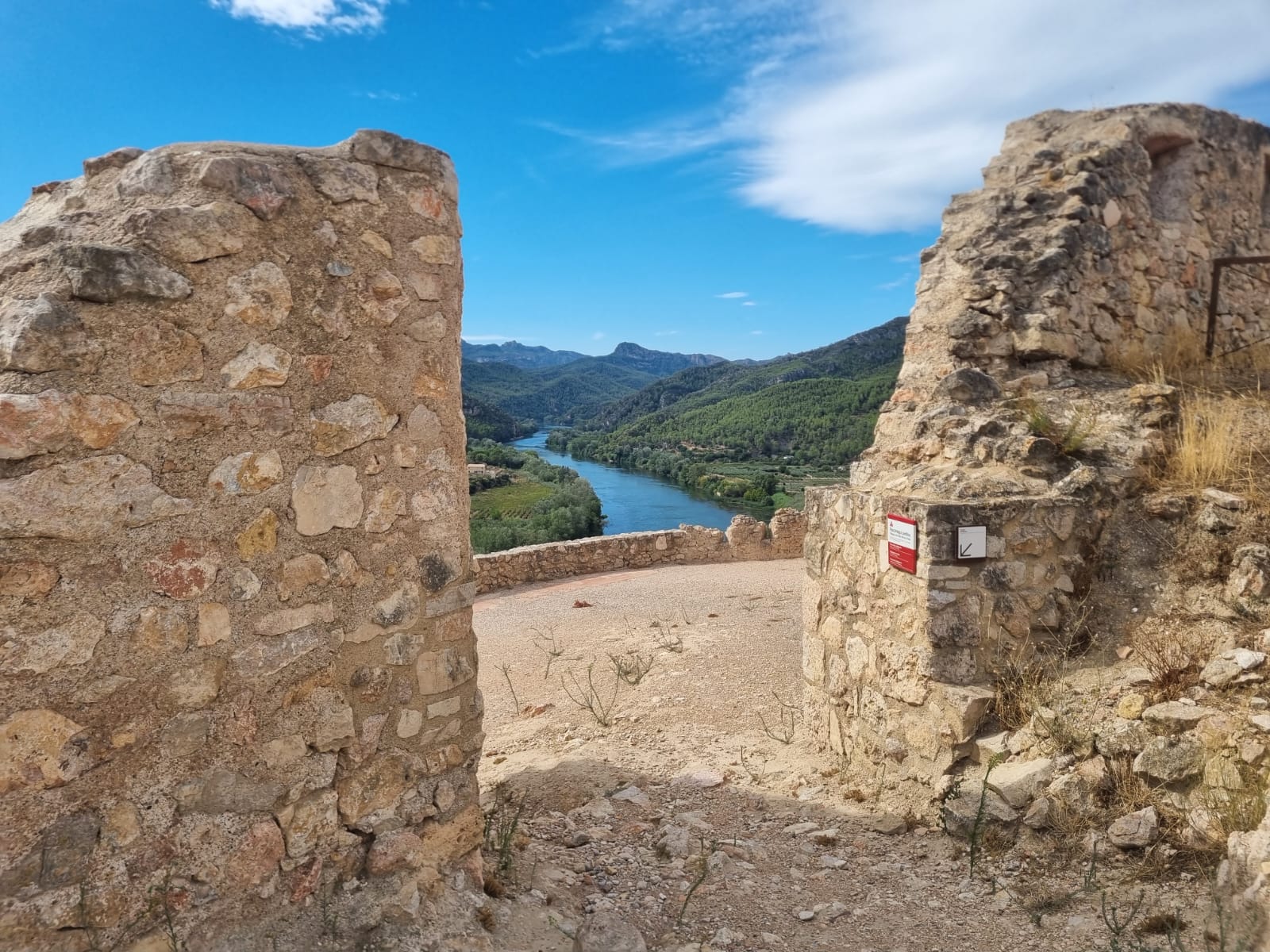 Vista de la terrassa sud del castell a través del pas de la muralla. Al fons, el riu Ebre baixa entre turons coberts de vegetació.