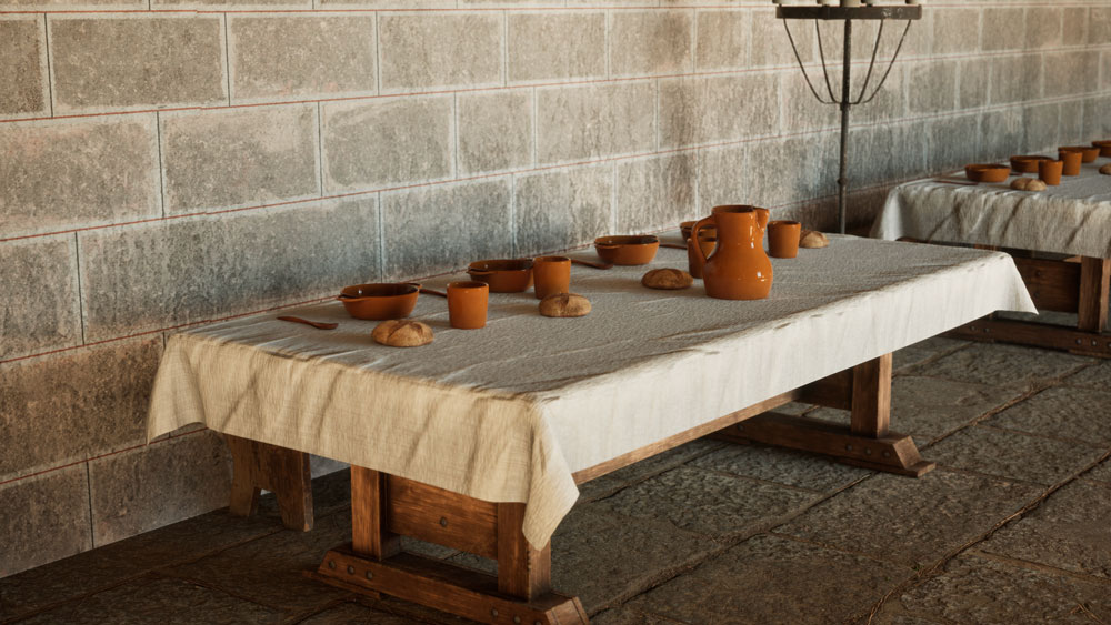 Detall d’una taula parada del refetor del castell. Hi ha servei per a quatre comensals: plats, gots i una gerra —tot de ceràmica marró esmaltada—, culleres de fusta i un panet per cap. Les tovalles són de teixit natural.