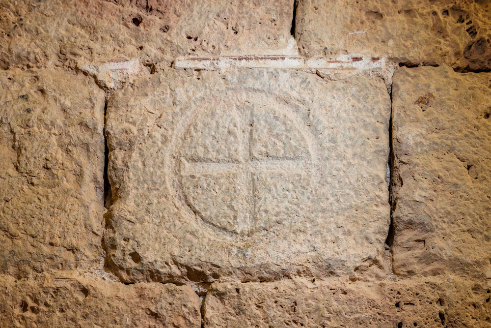 Detall d’una creu de consagració gravada a la pedra del mur de l’església del castell, inscrita a l’interior d’un cercle igualment gravat